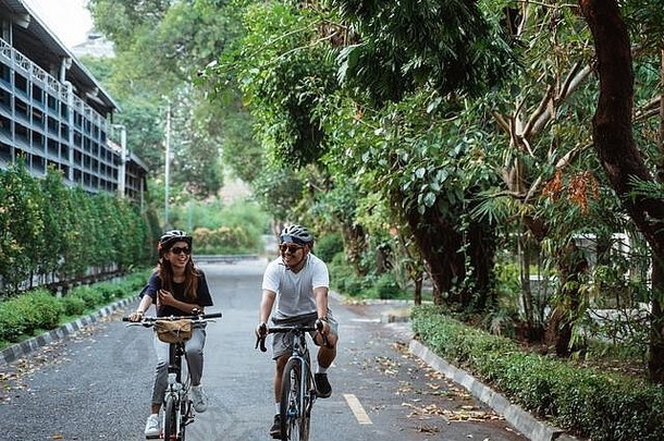 戴头盔的亚洲年轻夫妇喜欢在公园里一起骑自行车