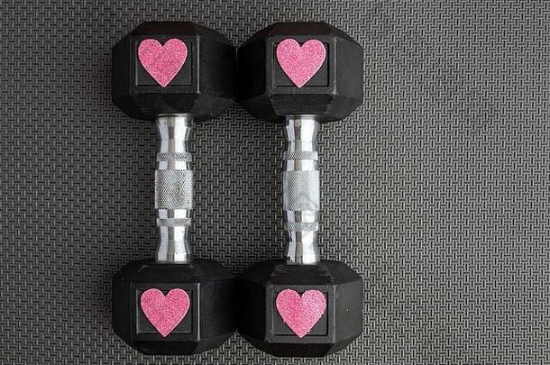 黑色健身房地板上的一对15磅重的哑铃，粉色闪亮的心形