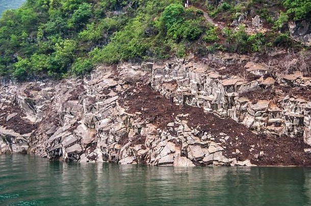中国武昌——2010年5月7日：大宁河上的龙门峡。灰白色岩石海岸线的特写镜头，上面覆盖着棕色的泥土和绿色的树叶