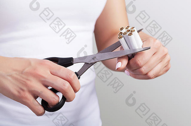 控制吸烟的概念。手里拿着剪刀。剪刀剪断了许多香烟。反对吸烟，保护健康。在灰色背景上。