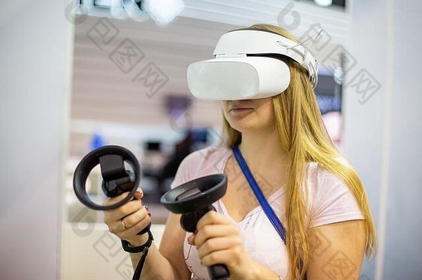戴着虚拟现实头盔的年轻白人女孩手里拿着控制棒，玩着一个游戏，特写，软焦点，背景模糊。