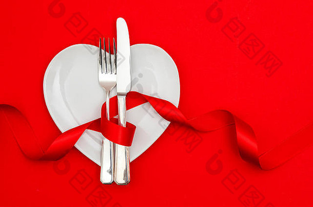 情人节晚餐的概念。红色背景上有刀叉的心形盘子