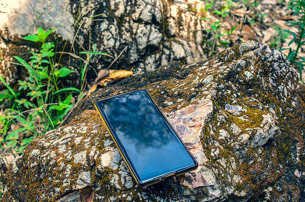 智能手机与石头和自然。岩石上的空手机和热带自然