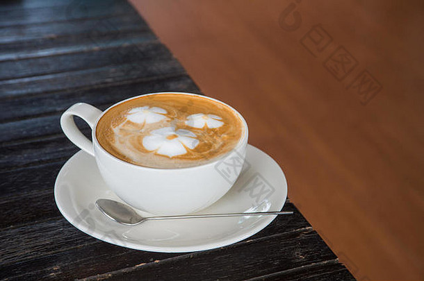 在木制背景上的白色杯子里放一杯有花图案的咖啡。