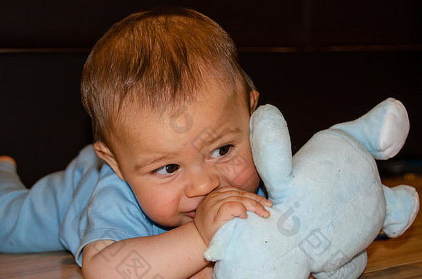 可爱的六个月大的小男孩在地板上玩蓝色的泰迪熊，出牙和早期发育的概念