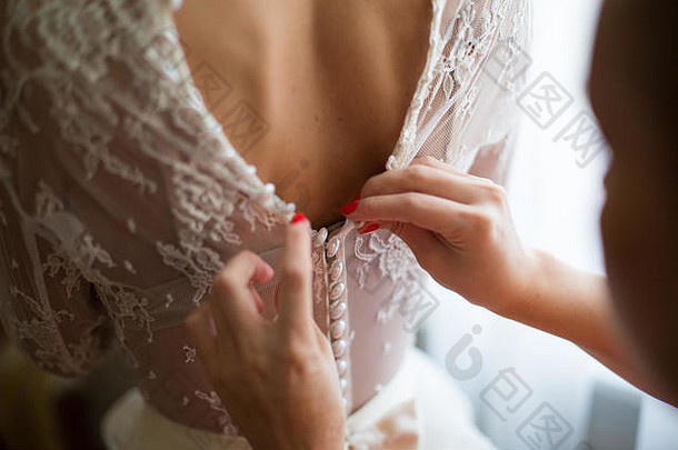 从后面看新娘。伴娘拉上婚纱的拉链。