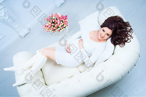 一位孕妇躺在沙发上，旁边有一个盛着郁金香的篮子