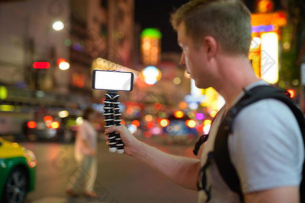 夜间，一名游客手持手机在唐人街闲逛