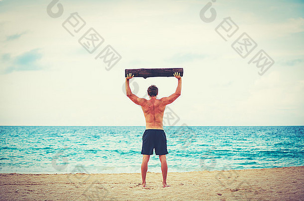 CrossFit海滩训练。男子运动员在海滩上用圆木做户外运动。健康的生活方式。