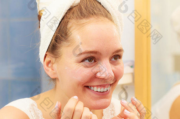 女人在浴室的脸上涂面膜保湿护肤霜。女孩在护理她的肤色，使用分层保湿霜。护肤水疗。