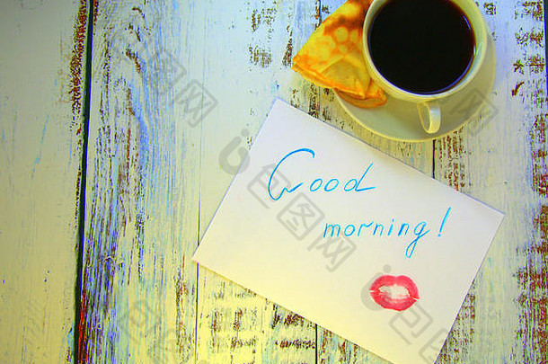 一杯咖啡，一个新烤的煎饼和一张纸，上面有一个早上好的愿望和一点<strong>口红</strong>。特写。