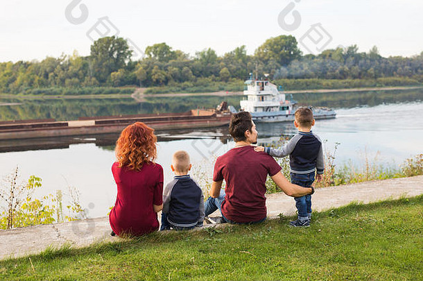 亲子关系、童年和自然概念——一家人坐在绿色的地面上看着小船