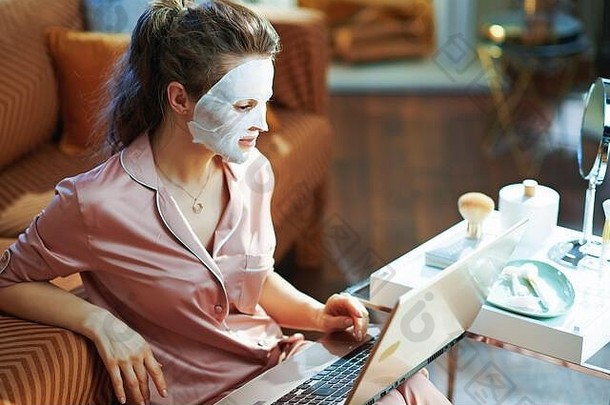 优雅的中年家庭主妇穿着睡衣，白床单面具，梳妆台上的镜子，现代生活中的笔记本电脑