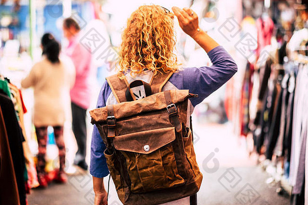 金发卷发的女背包客旅行者在<strong>二手市场</strong>从后面观看，享受购物和其他度假之旅-皮革背包
