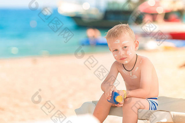 可爱的小男孩在海滩上拿着一瓶<strong>防晒乳</strong>液，身上涂着<strong>防晒</strong>霜