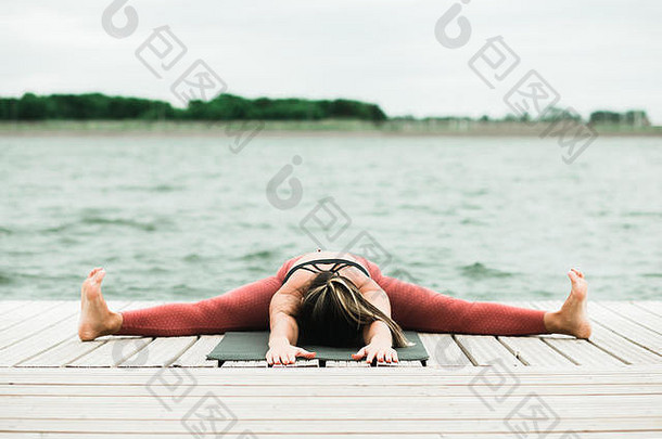在湖边的码头上做瑜伽的亚洲女孩。她穿着黑色上衣和红色紧身裤。