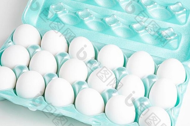 一个明亮的绿色泡沫塑料板条箱的特写镜头，里面装满了白色鸡蛋，背景是白色的。