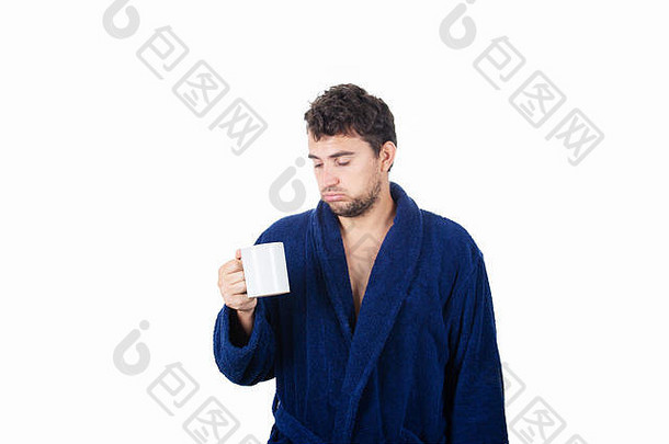 肖像伤心困了年轻的男人。混乱的头发穿蓝色的浴袍喝咖啡杯孤立的白色背景