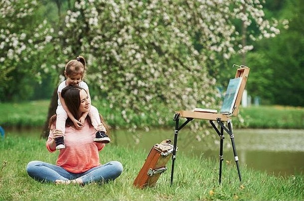 欣赏绘画。春天，母亲和女儿坐在公园的画架旁