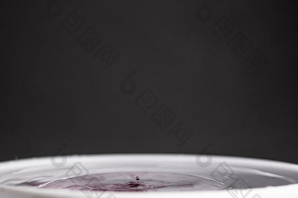 一个紫色水滴溅入水中的特写微距照片，背景为深灰色