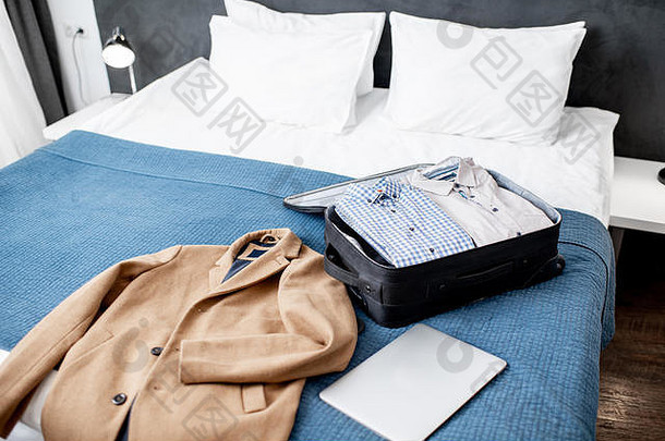 装满衣服和外套的手提箱放在酒店房间或卧室的床上。商务旅行概念