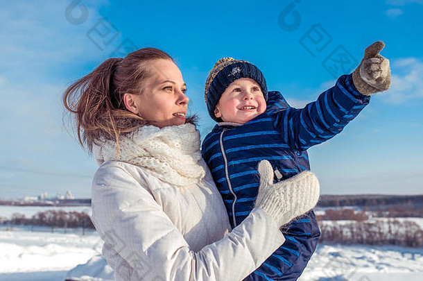 一个小男孩，一个孩子在一位年轻母亲的怀里，把手伸到头顶。穿着蓝色工作服和帽子。一位妇女抱着一个孩子。