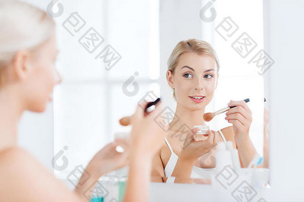 在浴室拿着化妆刷和化妆粉的女人