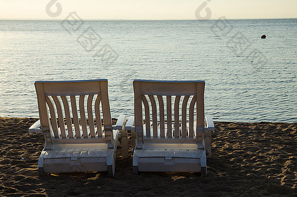 傍晚阳光下海滩边的两把空扶手椅