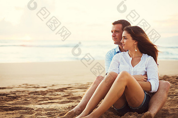 一对幸福的年轻情侣在海滩上看日落。假期蜜月度假。