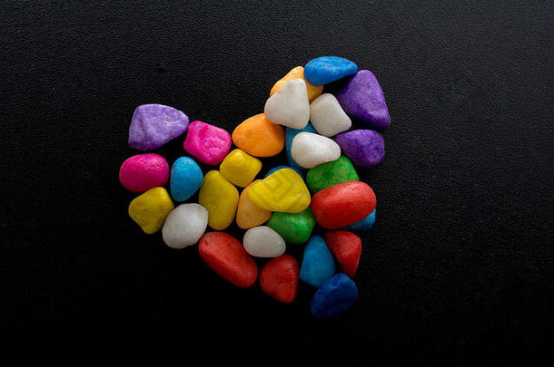 五颜六色的小鹅卵石在黑色岩石上形成心形