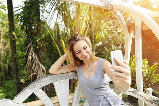 泰国普吉岛，阳光明媚的日子里，一名<strong>女子</strong>用智能手机自拍，背景是阳光绿的棕榈树