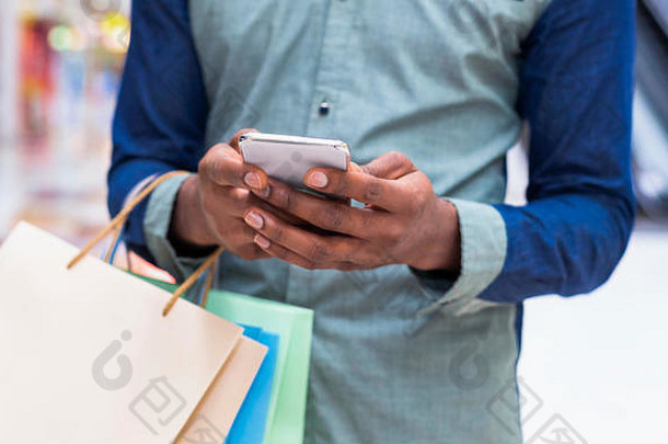 一个拿着购物袋用手机的非洲男人