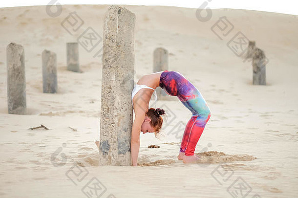 一位瑜伽修行者或瑜伽大师导师在日出时在海滩上锻炼，并在清晨展示她的力量、控制力和技巧。