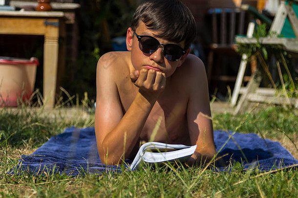 十几岁的男孩阅读书日光浴花园穿太阳镜