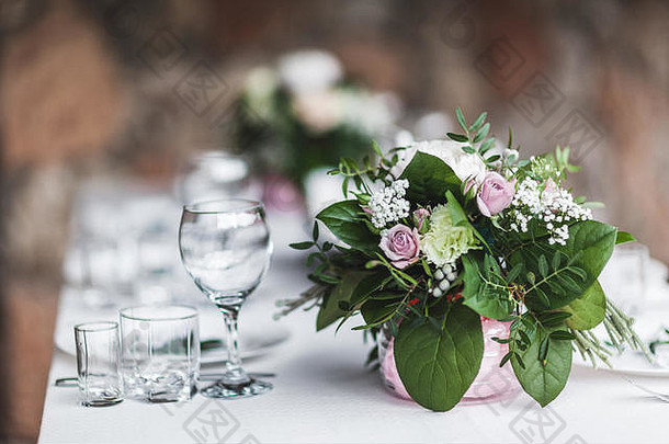 白色的婚宴桌上装饰着绿色的鲜花，名片，粉色的牡丹花，白色的餐具，乡村风格