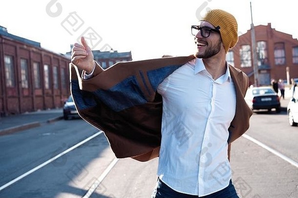 时尚男士肖像。一个戴眼镜、穿着外套的年轻人走在街上。