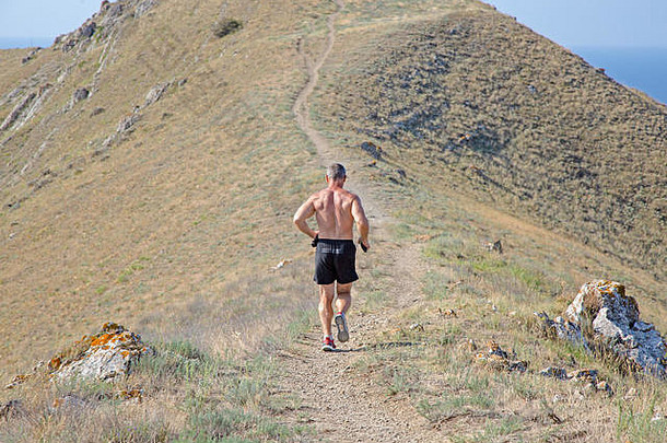 在蓝天背景下的山路上跑步的运动员的后视图