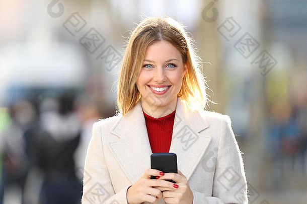 冬天，一个穿着外套的女人在街上摆好姿势看着你拿着一部智能手机