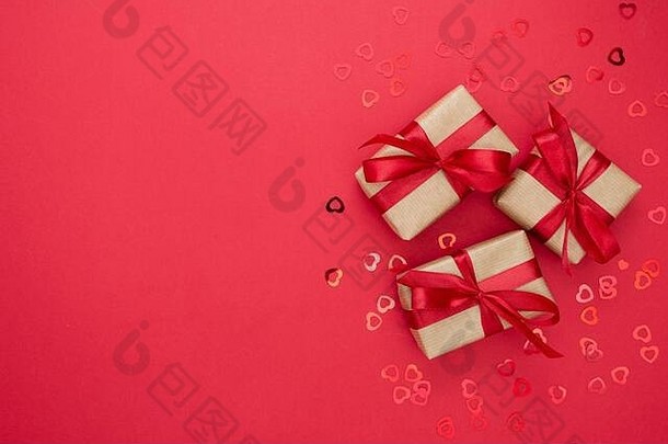 用牛皮纸包装的礼品盒和红色背景上隔离的红结。抽象平铺。
