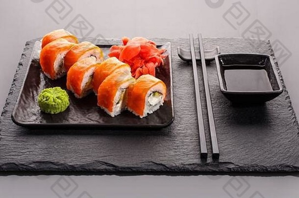 深色石头背景上的日本寿司。寿司配生姜、芥末和酱油。用筷子吃。