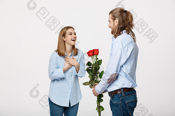 这位英俊优雅的男子的肖像画以红玫瑰和白色孤立背景上的微笑让他美丽的女友大吃一惊。