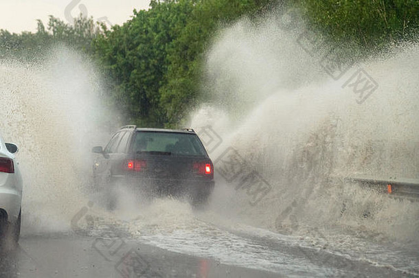 大雨时汽车撞上了一个大水坑，水溅到了汽车上。雷雨天气，汽车在柏油路上行驶。危险驾驶条件