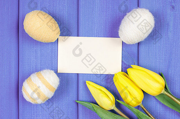新鲜的黄色郁金香和复活节彩蛋用羊毛线包裹在木板上，在纸上留下文字或铭文的空间