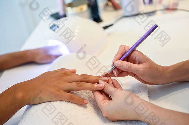 美容师在一家美甲沙龙用刷子为一名妇女画指甲的特写镜头。正在修指甲的顾客。