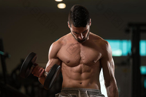 年轻肌肉发达的男子在健身房用哑铃练习二头肌