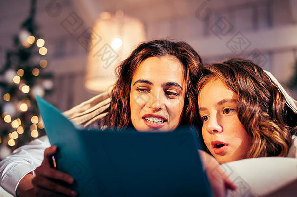 年轻漂亮的女孩们在圣诞节早上躺在床上，快乐的家庭在假日里微笑着阅读书籍