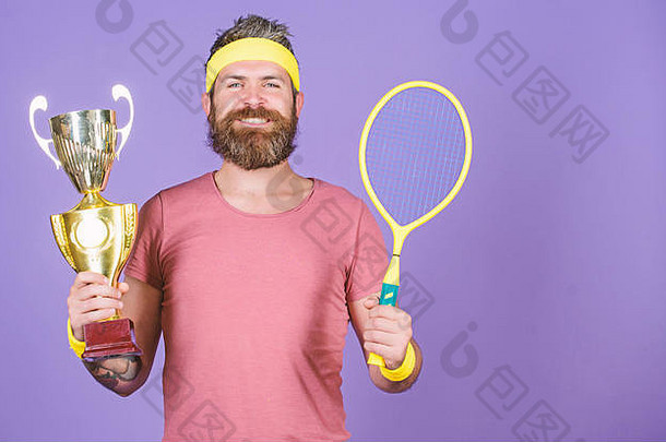 体育成就。庆祝胜利。网球冠军。运动健将拿着网球拍和金高脚杯。赢得网球比赛。网球运动员赢得冠军。留着大胡子的成功运动员。第一名。