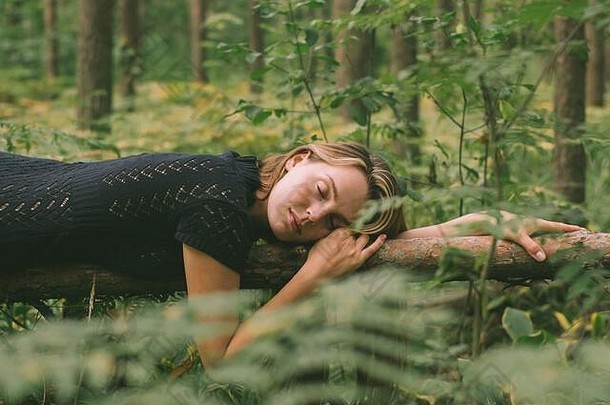 在森林里，一个穿着黑衣服的年轻漂亮女孩躺在树干上，闭着眼睛