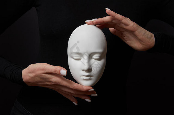 两个女人的手拿着黑色背景上的白色石膏面具。<strong>社会心理</strong>面具概念