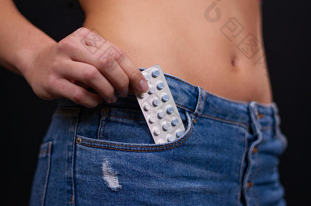 漂亮苗条的少女，穿着紧身牛仔裤，口袋里放着避孕药，这表明她宁愿现在还不怀孕。